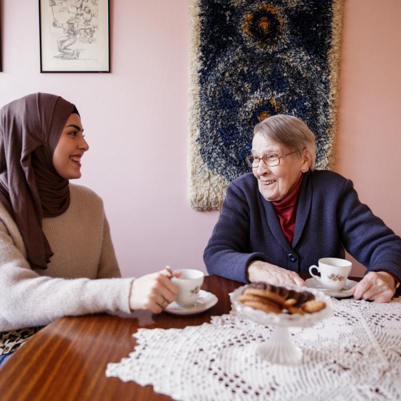 A younger and older woman are having a cup of coffee together at a table.